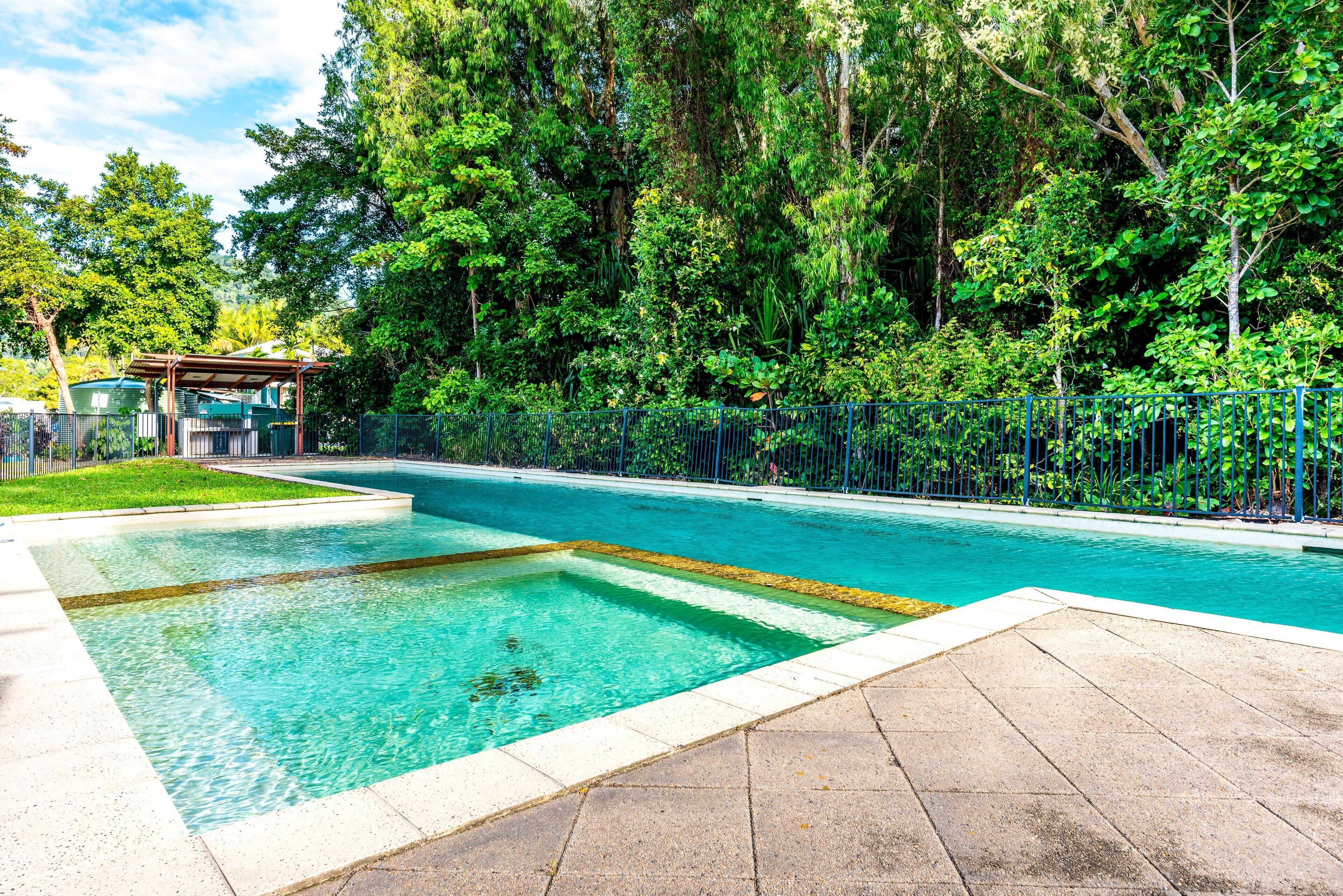 Ein rechteckiger Swimmingpool mit klarem, blauem Wasser, umgeben von einer gepflasterten Liegefläche und einem blauen Zaun.