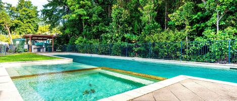 Ein rechteckiger Swimmingpool mit klarem, blauem Wasser, umgeben von einer gepflasterten Liegefläche und einem blauen Zaun.