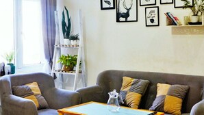 A living room with a grey sofa, a coffee table, and a ladder shelf with plants. - HANZ Chuong Hotel Da Lat (Xuan Huong - Da Lat)