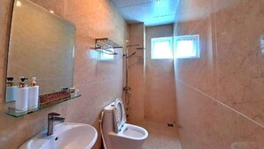 A bathroom with a sink, toilet, and shower. There is a mirror above the sink and a shelf with toiletries. - HANZ Chuong Hotel Da Lat (Xuan Huong - Da Lat)