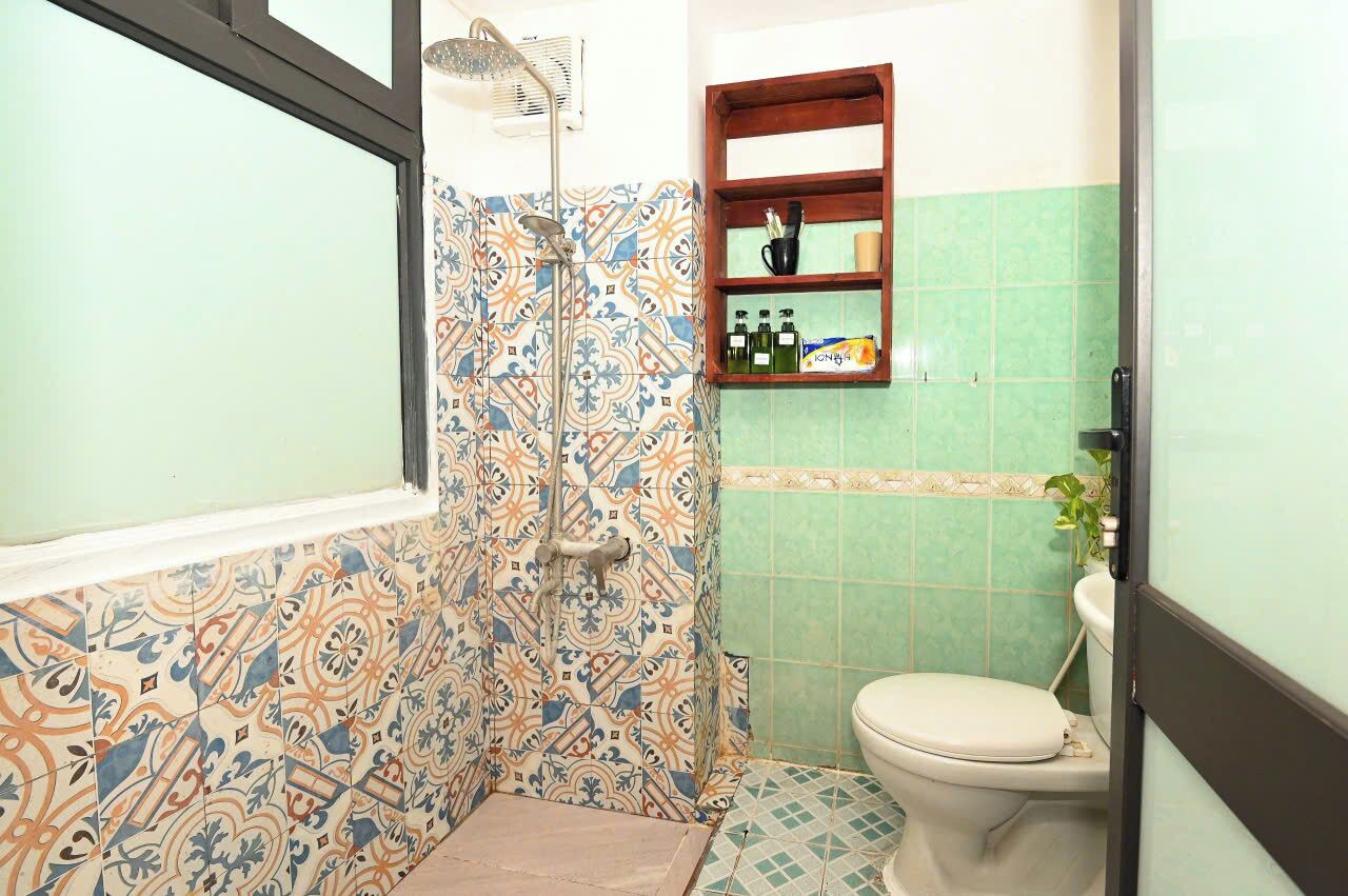 A bathroom with patterned tiles, a shower, a toilet, and a shelf with toiletries.
