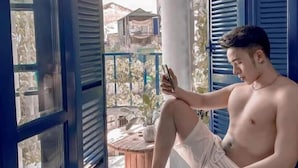 A person sitting on a balcony with a view of a building and plants.