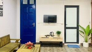 A room with a blue door, a television mounted on the wall, a wooden bench, a small table with a plant, and a potted plant near the door.