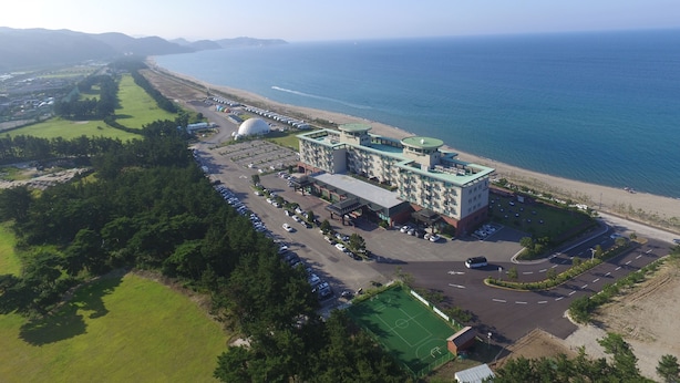 An aerial view of a coastal hotel with a parking lot, a beach, and a large dome structure. - Seaspovill Resort (Samcheok)