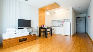 A modern living room with a wooden floor, a flat-screen TV, a dining area with a table and chairs, and a kitchen with white cabinets. - Seaspovill Resort (Samcheok)