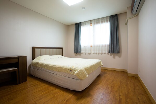 A bedroom with a bed, a desk, and a window with curtains.