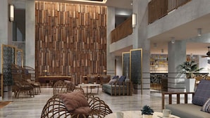 Un vestíbulo espacioso con techos altos, una pared central de madera con intrincados grabados y una variedad de zonas de estar, incluyendo sillones de mimbre y sofás.