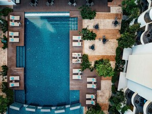 Luchtbeeld van een hotel met een groot zwembad, meerdere loungegedeeltes met stoelen en tafels, en omliggend groen.