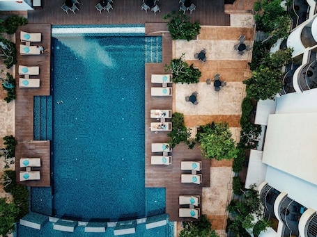 An aerial view of a hotel with a large swimming pool, multiple lounge areas with chairs and tables, and surrounding greenery.. Mercure Langkawi Pantai Cenang