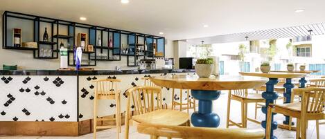 Un espace bar moderne avec des chaises et des tables en bois, un comptoir où sont exposées différentes bouteilles et un sol carrelé.