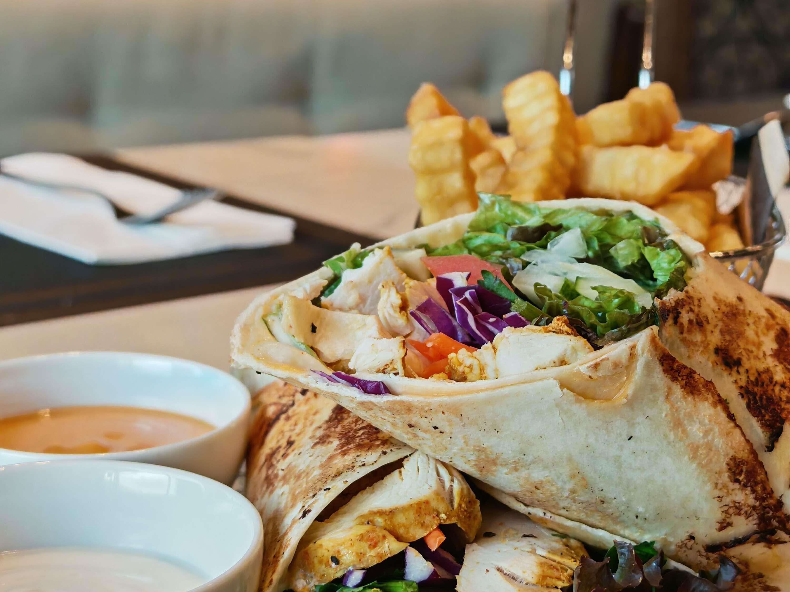 A wrap with chicken, vegetables, and sauce, accompanied by fries and two dipping sauces.