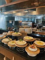 Montaje de buffet con diferentes platos y una cocina al fondo.