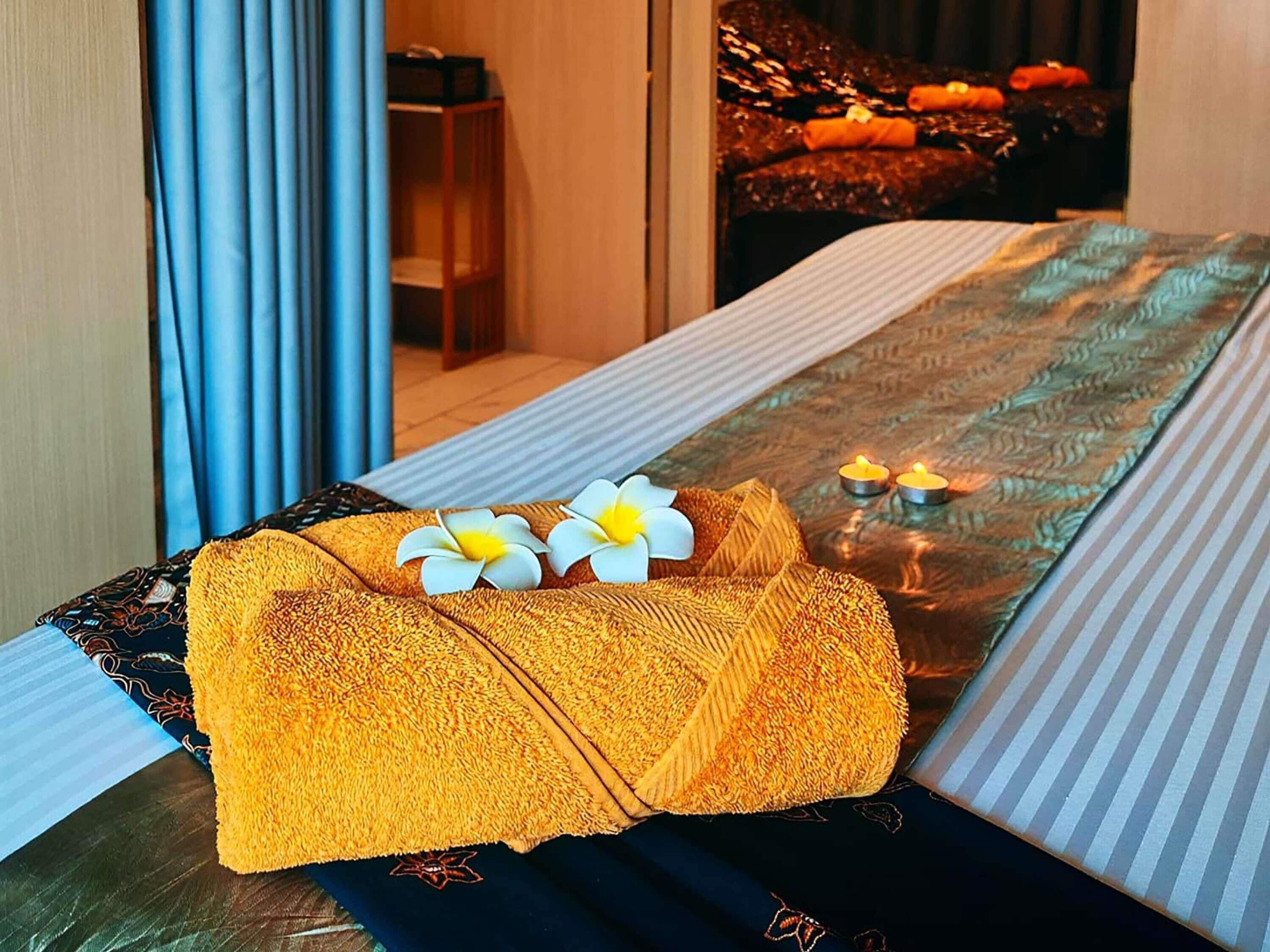 Een net opgemaakt bed met een gestreept dekbedovertrek, een opgevouwen handdoek en twee witte bloemen.