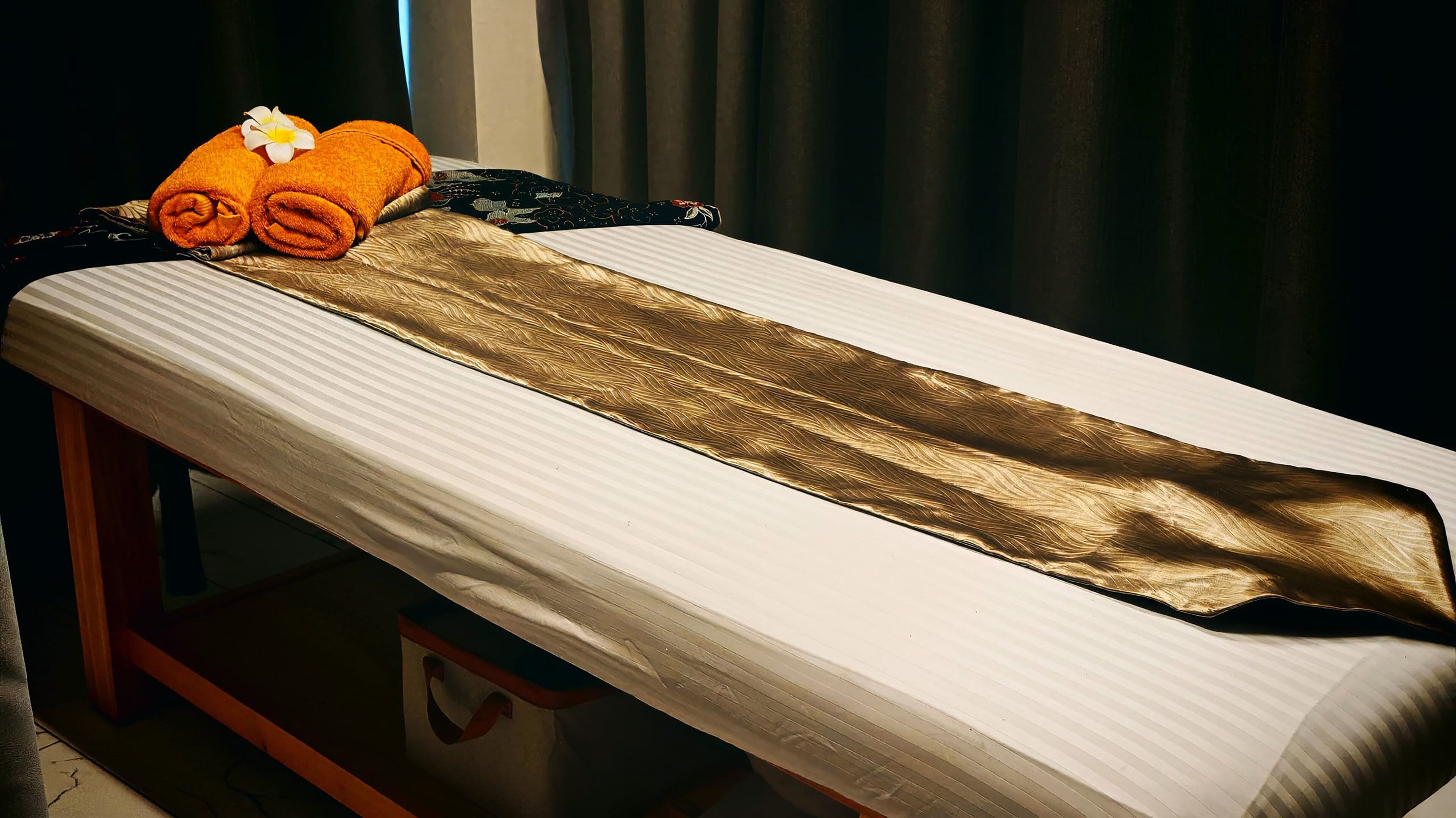 A massage table with a white sheet and a gold-colored towel.