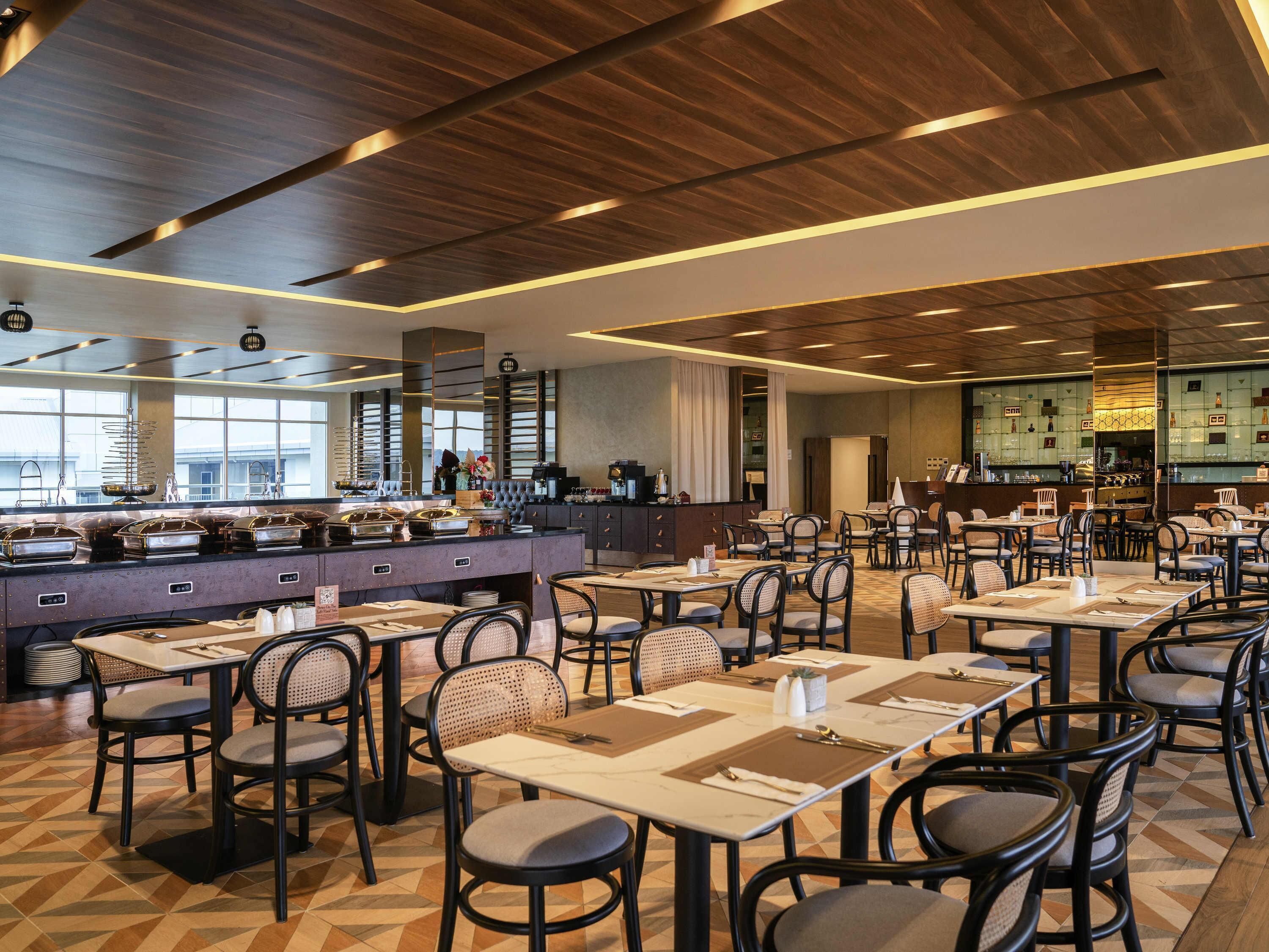 Een ruime eetruimte met meerdere tafels en stoelen, een buffet en een keuken op de achtergrond.