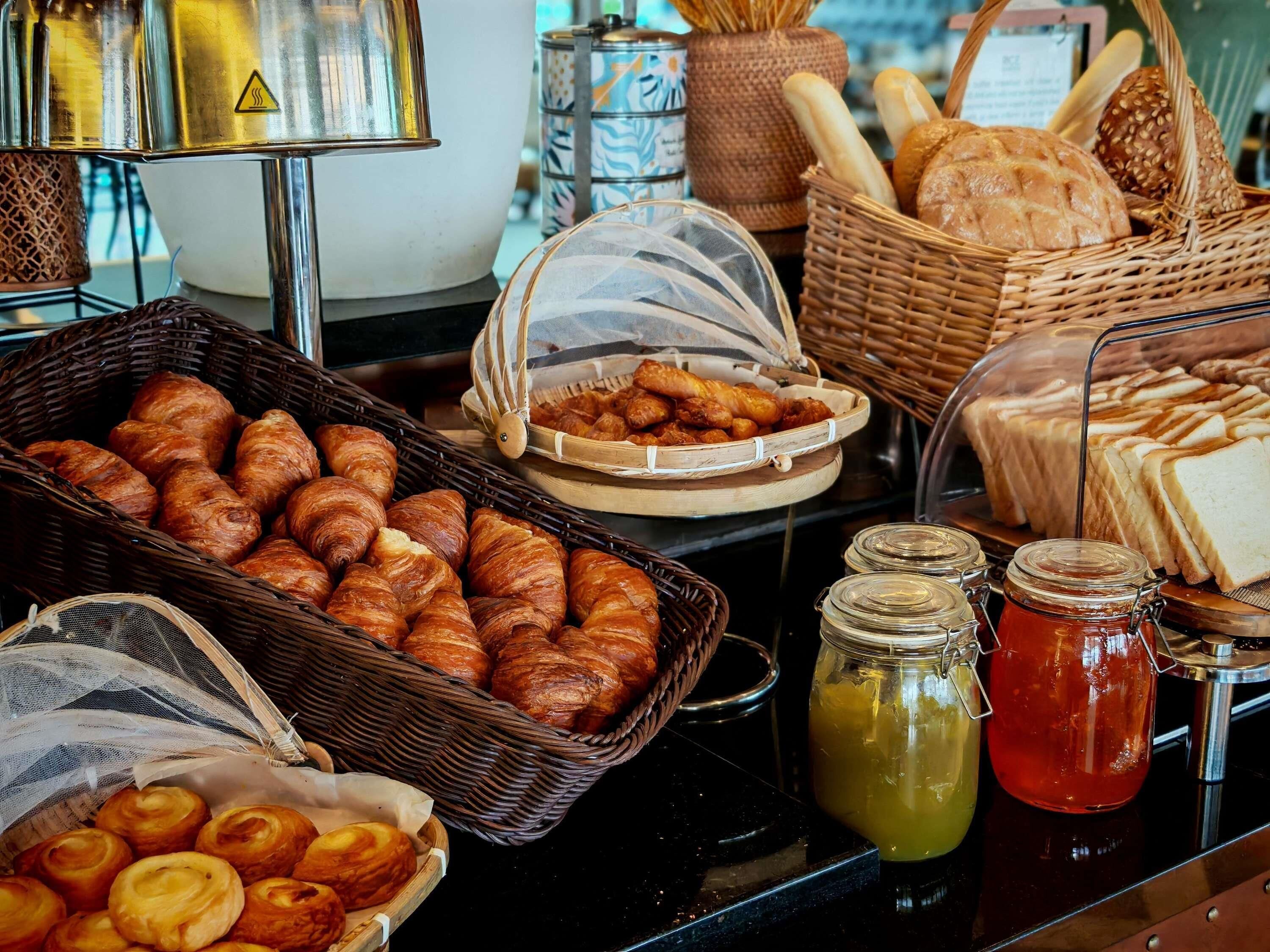 A buffet with various baked goods, including croissants and bread, and two jars of condiments.