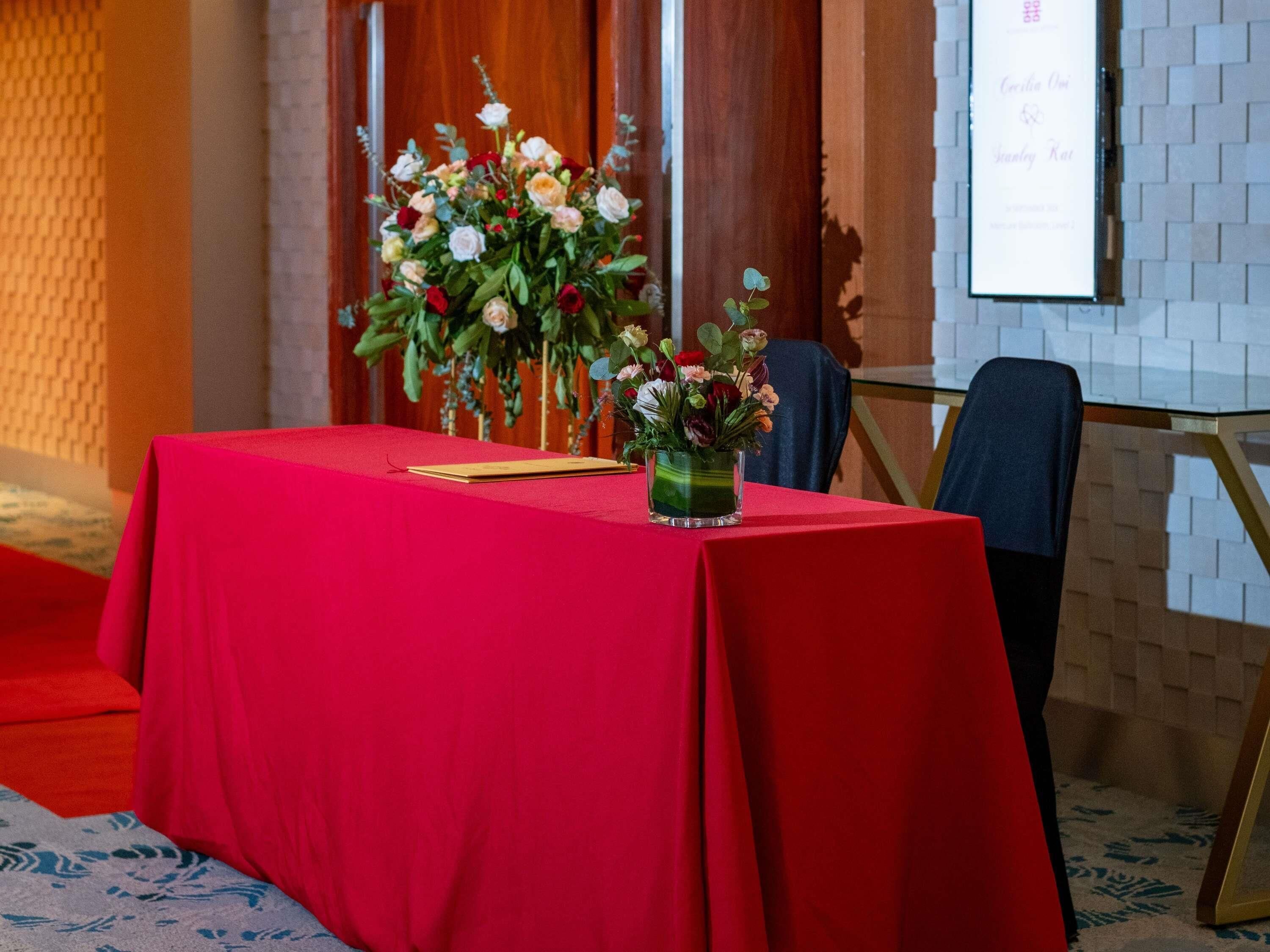 A table with a red tablecloth, a vase of flowers, and a framed picture on the table.