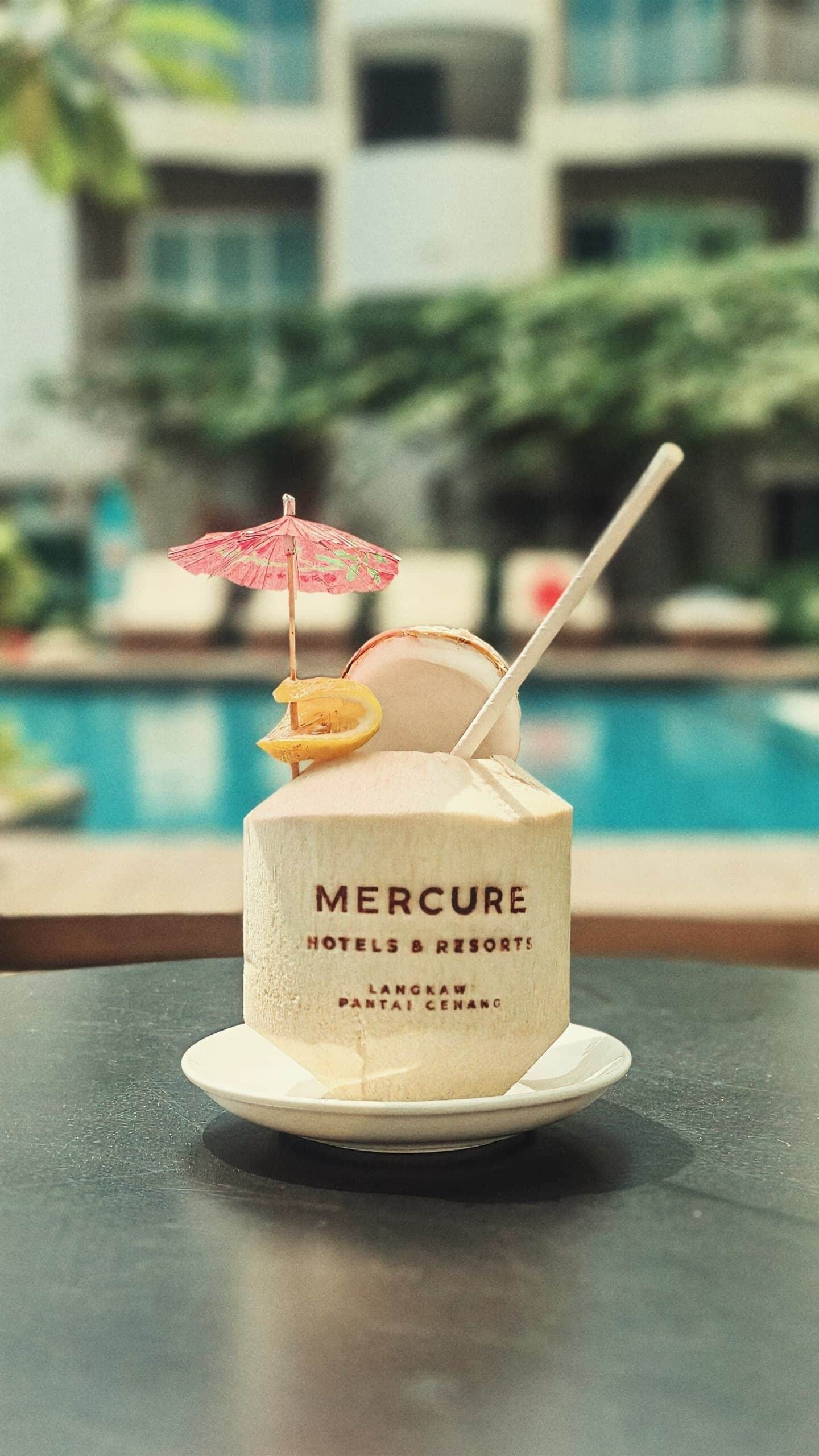 Una bebida de coco con una pajita y una rodaja de limón encima, con la etiqueta 'MERCURE HOTELS & RESORTS LANGKAW PANTAI PENANG'.