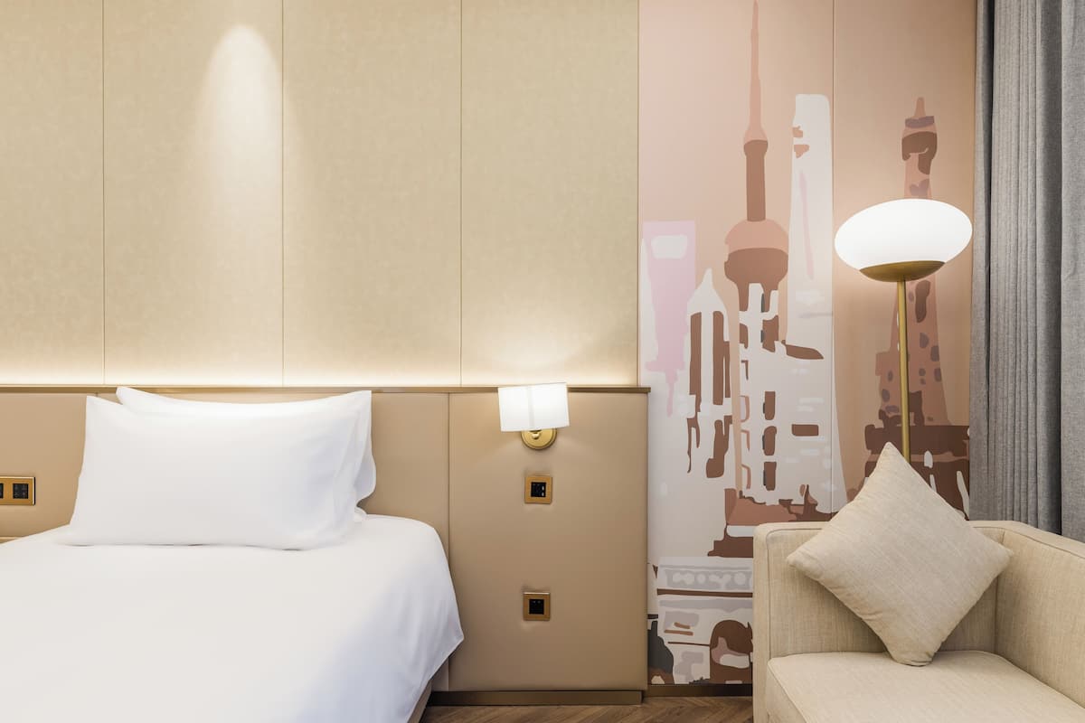 Quarto de hotel com cama, sofá, luminária na parede e um mural.