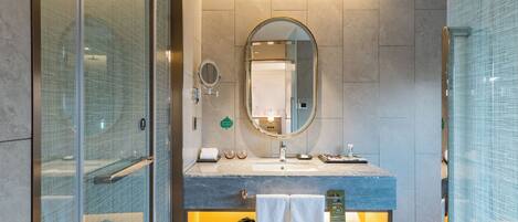 A modern bathroom with a glass shower enclosure, a round mirror, a sink with a marble countertop, and a towel rack.