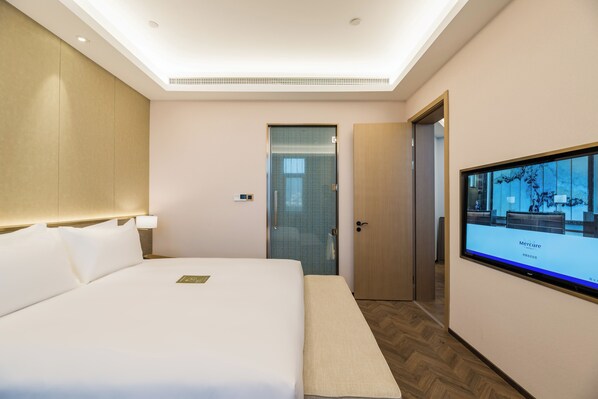 Una habitación de hotel con una cama grande, un televisor en la pared, una puerta y un banco.
