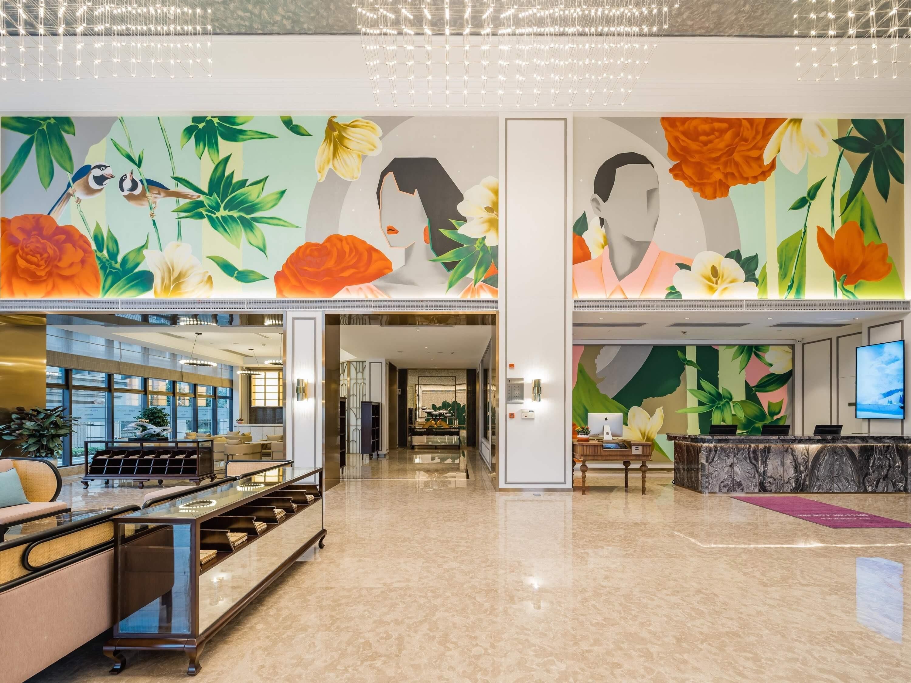 Un hall amplio con mostrador de recepción, zona de estar y un gran mural con motivos florales y de aves.