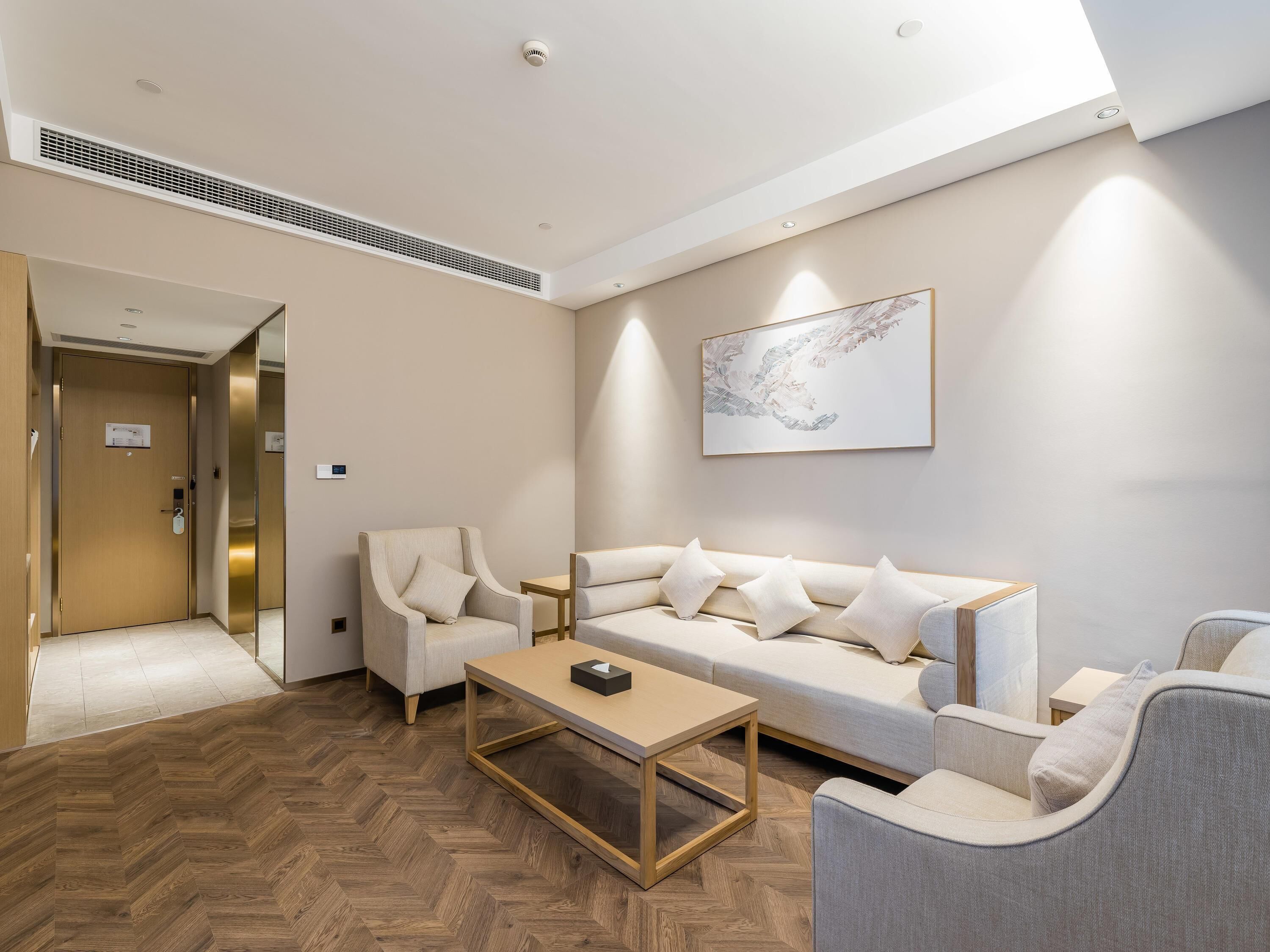 Una habitación de hotel moderna con piso de madera en patrón de espiga, un conjunto de sofás, una mesa de centro y una obra de arte abstracto colgada en la pared.