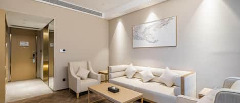 Una habitación de hotel moderna con piso de madera en patrón de espiga, un conjunto de sofás, una mesa de centro y una obra de arte abstracto colgada en la pared.