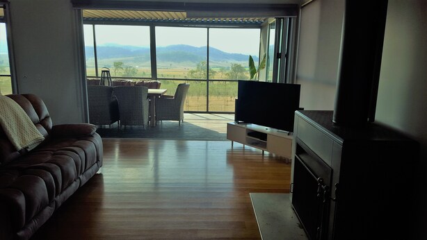 Un salon avec un canapé, un téléviseur et une vue sur un paysage, visible à travers de grandes fenêtres.
