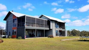 Une maison moderne à deux étages, dotée de grandes fenêtres, d’un balcon et d’une pelouse bien entretenue.