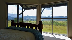 Une chambre dotée d’une grande fenêtre donnant sur un paysage rural, avec des champs et des montagnes à l’horizon.