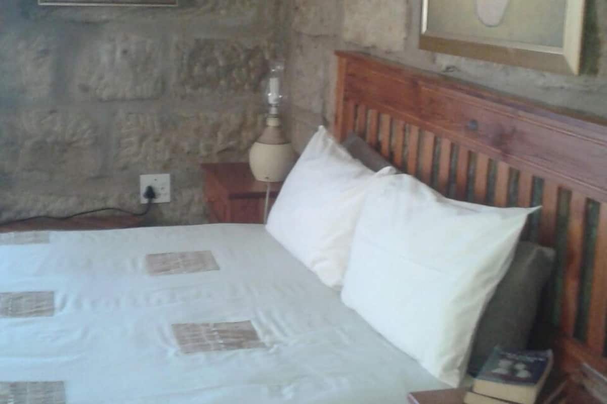 Ein Schlafzimmer mit Steinwand, einem Bett mit weißer Bettwäsche, einem Holz-Kopfteil, einem Nachttisch mit Lampe und einem gerahmten Bild an der Wand.