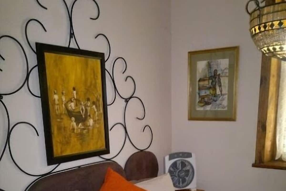 Ein ordentlich bezogenes Bett mit weißen und orangefarbenen Kissen, einem Wandkunstwerk und einem Bild darüber.