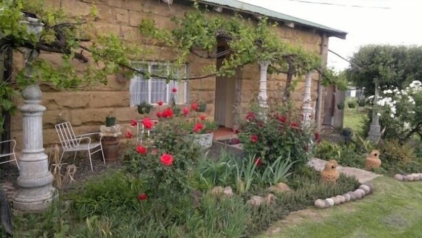 A stone house with a garden featuring red flowers and a pergola. - Rosenhof Country Lodge (Paul Roux)