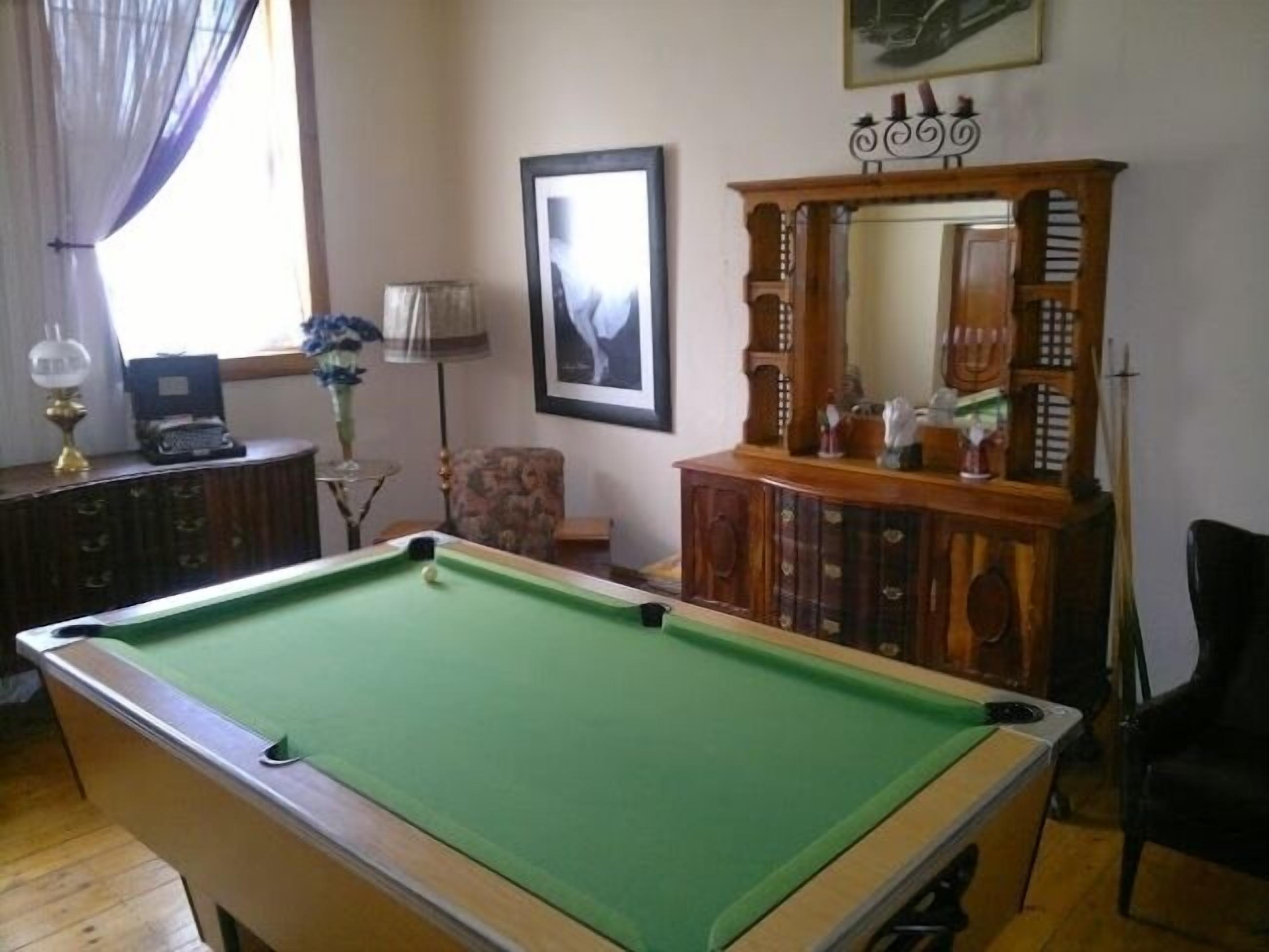 Una mesa de billar en una habitación con un mueble de madera, un cuadro en la pared y una lámpara.
