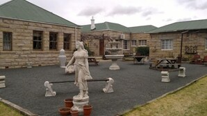 A courtyard with stone buildings, a statue, and outdoor seating. - Rosenhof Country Lodge (Paul Roux)