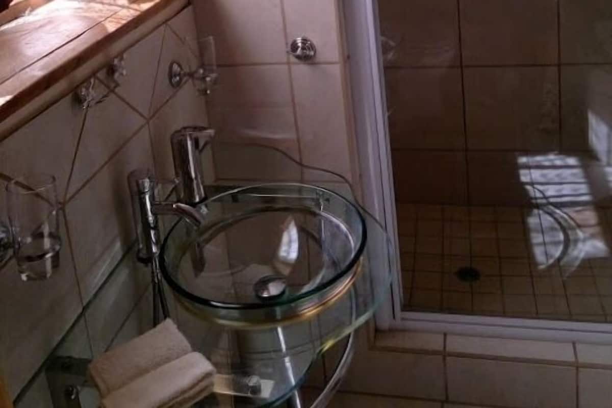 Ein Badezimmer mit einem Glaswaschbecken, einem Holzregal und einer Duschkabine.