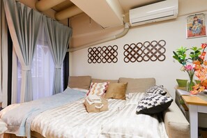 A hotel room with a bed, a bedside table with a vase of flowers, and a wall-mounted air conditioner. - Nishishinjuku Hana Apartment (Tokyo)