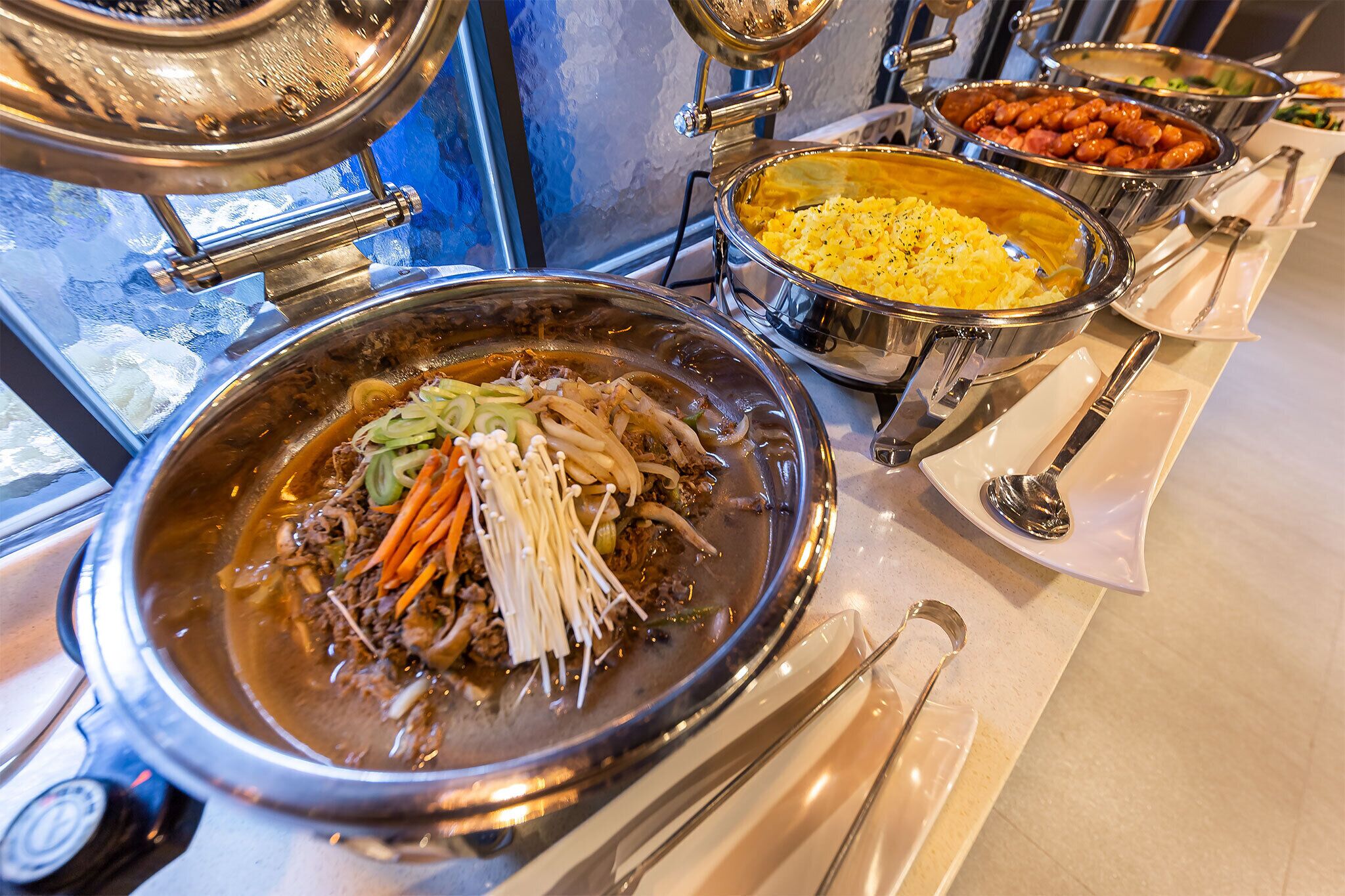 Un buffet proposant divers plats, notamment un plat mijoté avec des légumes et de la viande, ainsi que d’autres plats comme du riz et des haricots.