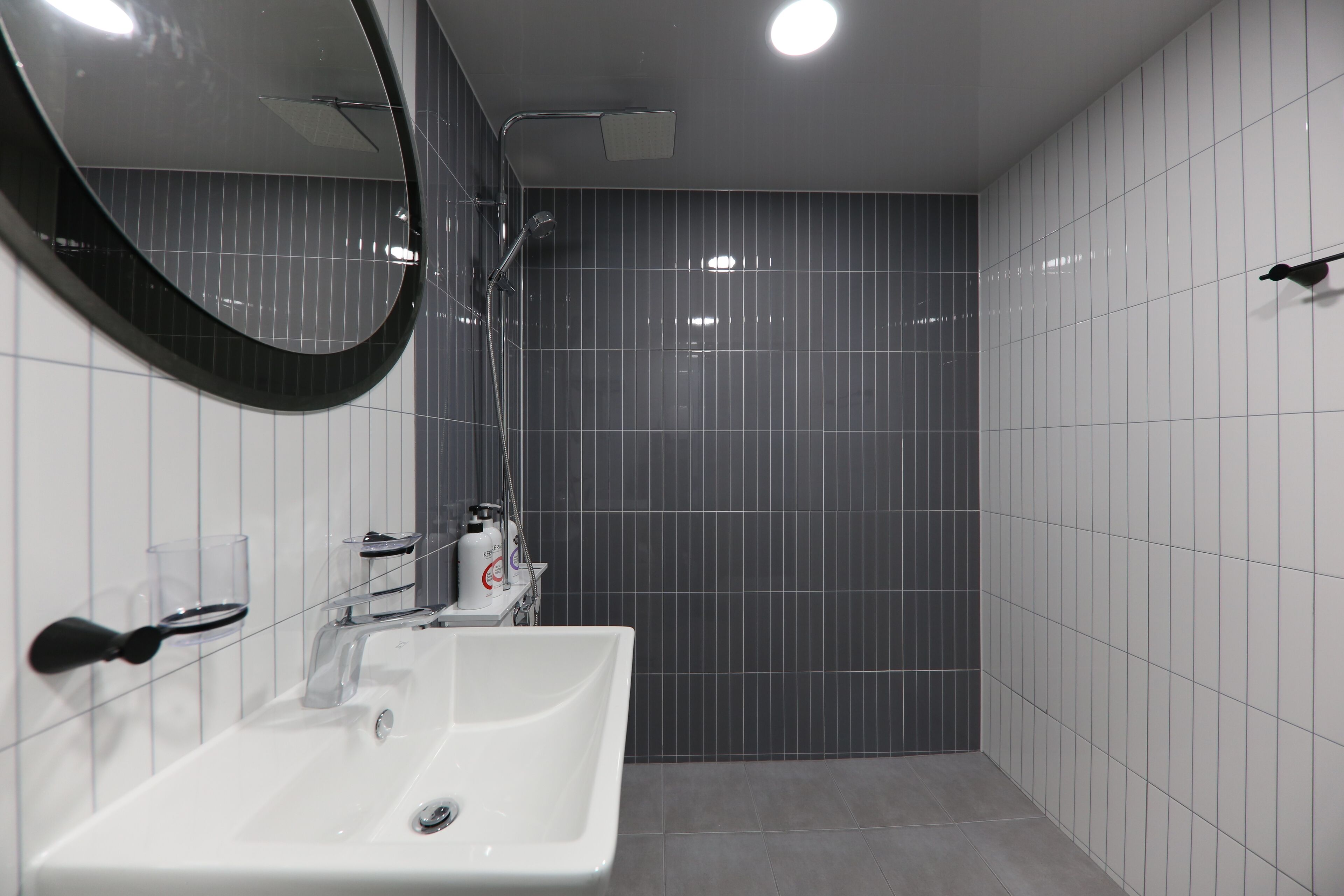 A modern bathroom with a white sink, a mirror, and a shower area.