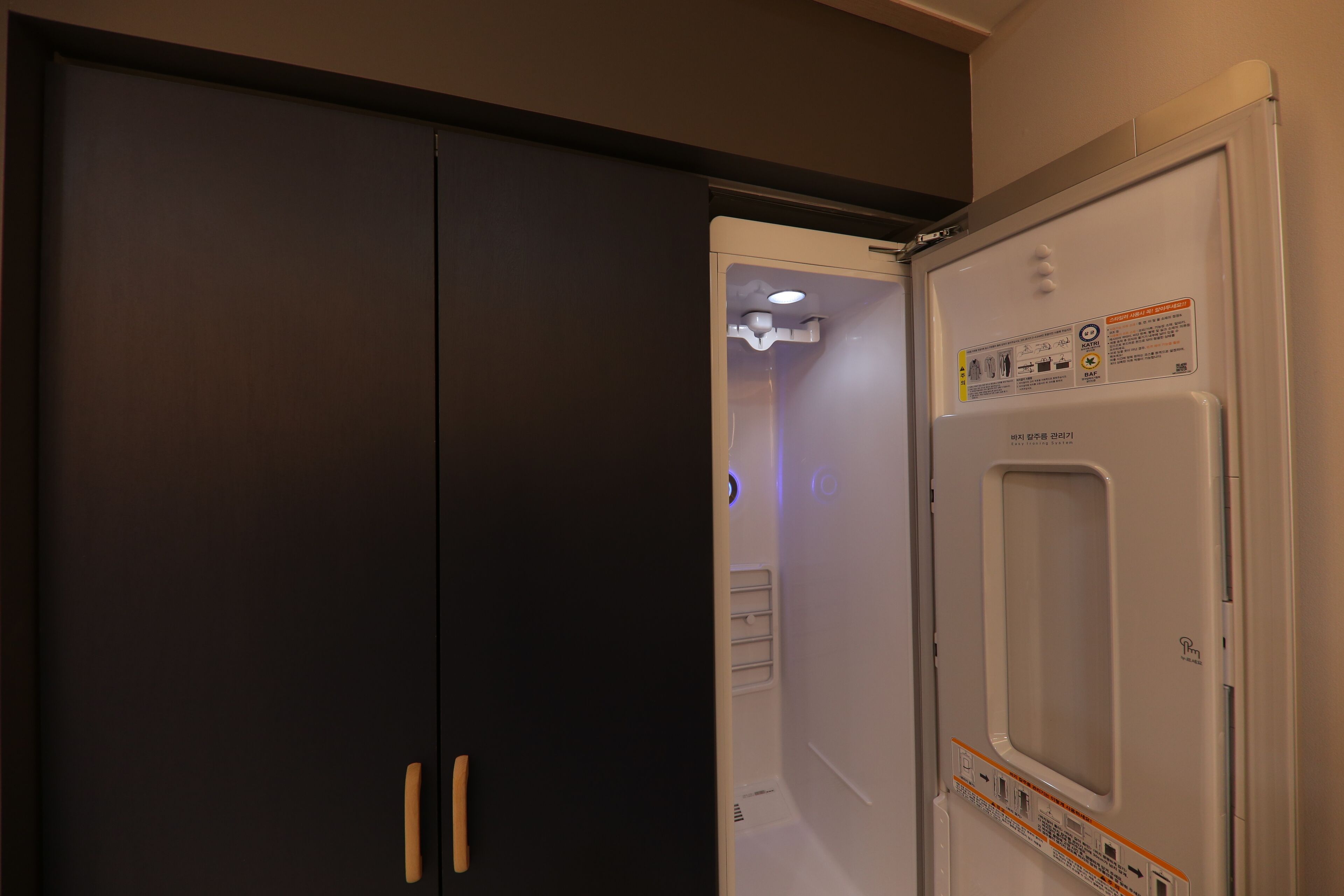 A room with a closed dark-colored wardrobe and a white refrigerator with a control panel.