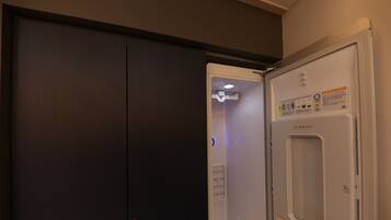 A room with a closed dark-colored wardrobe and a white refrigerator with a control panel.