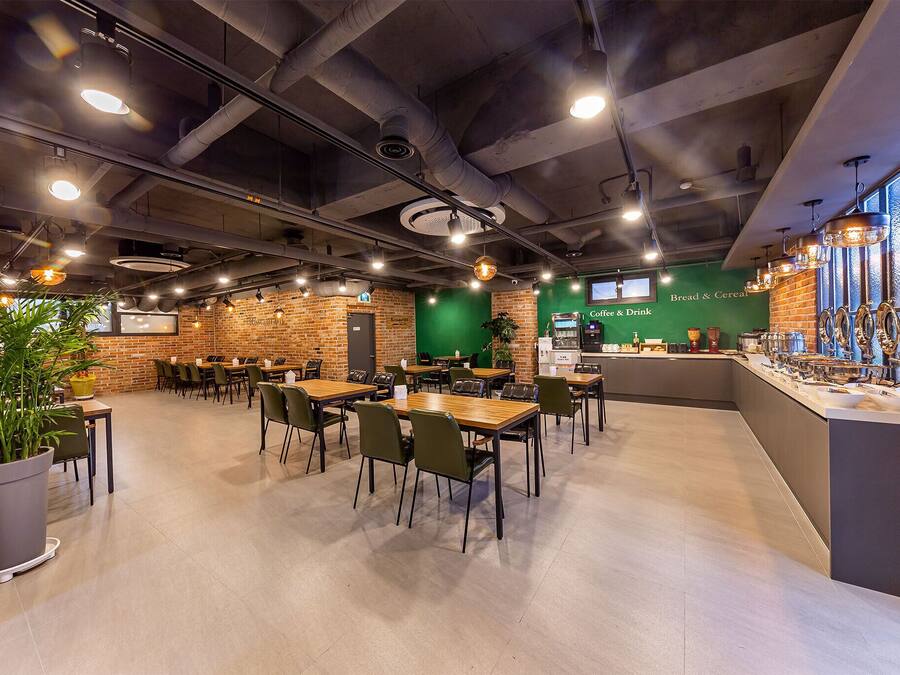 Un café moderno con paredes de ladrillo, varias mesas y sillas, una máquina de café y una barra con un letrero que dice "Coffee & Bread & Cereal".