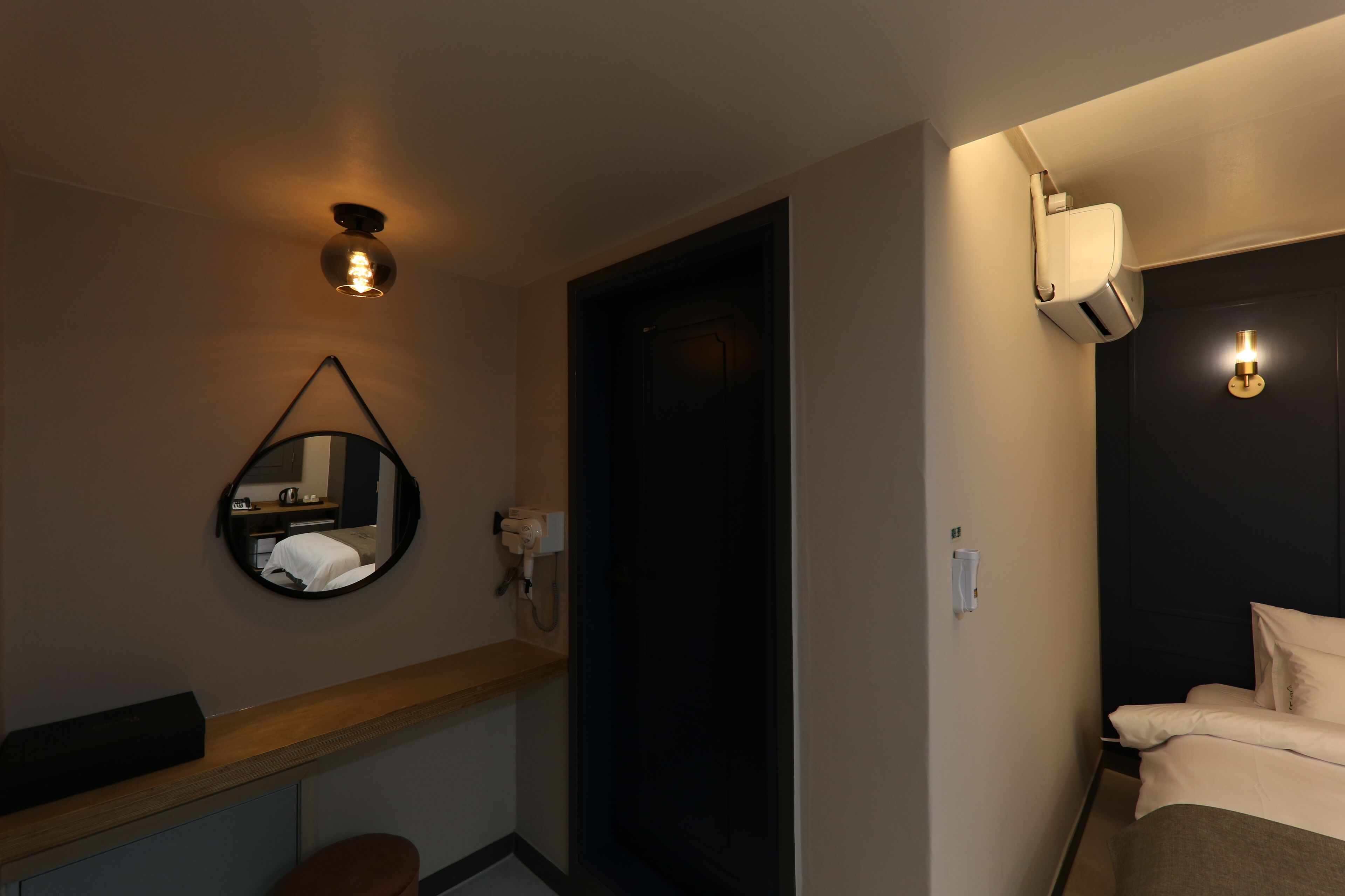 A hotel room with a bed, a round mirror, a small table, and a wall-mounted light fixture.