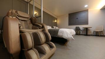A modern hotel room with a massage chair, a bed, a small table, and two chairs.