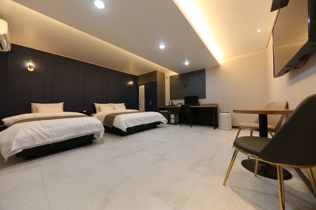 Una habitación de hotel moderna con dos camas, un escritorio, una silla y un televisor montado en la pared.