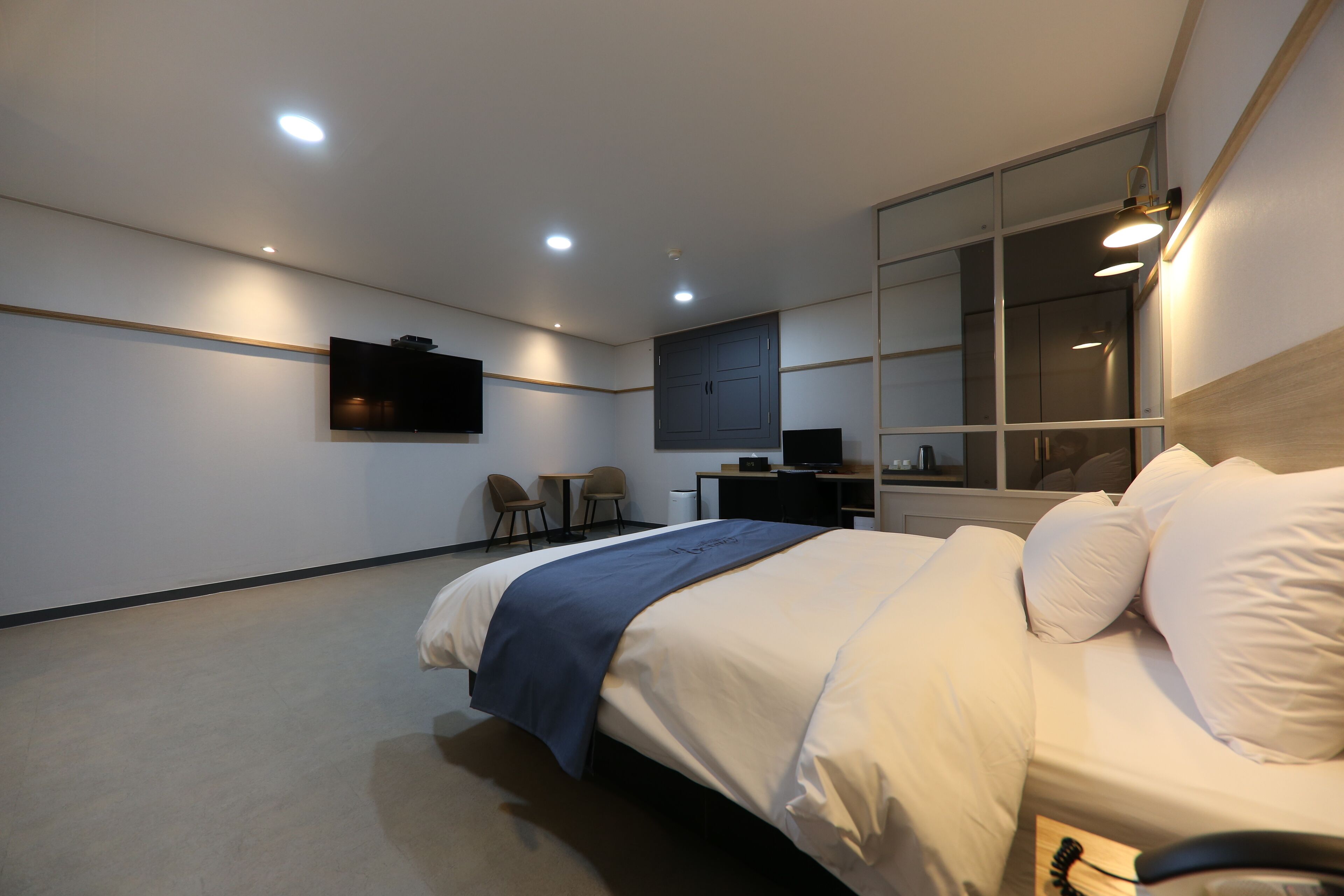A modern hotel room with a large bed, a desk, a chair, and a TV mounted on the wall.