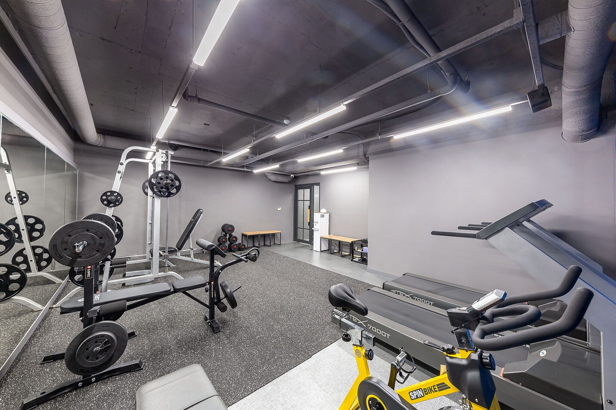 A gym with weightlifting equipment, cardio machines, and benches.