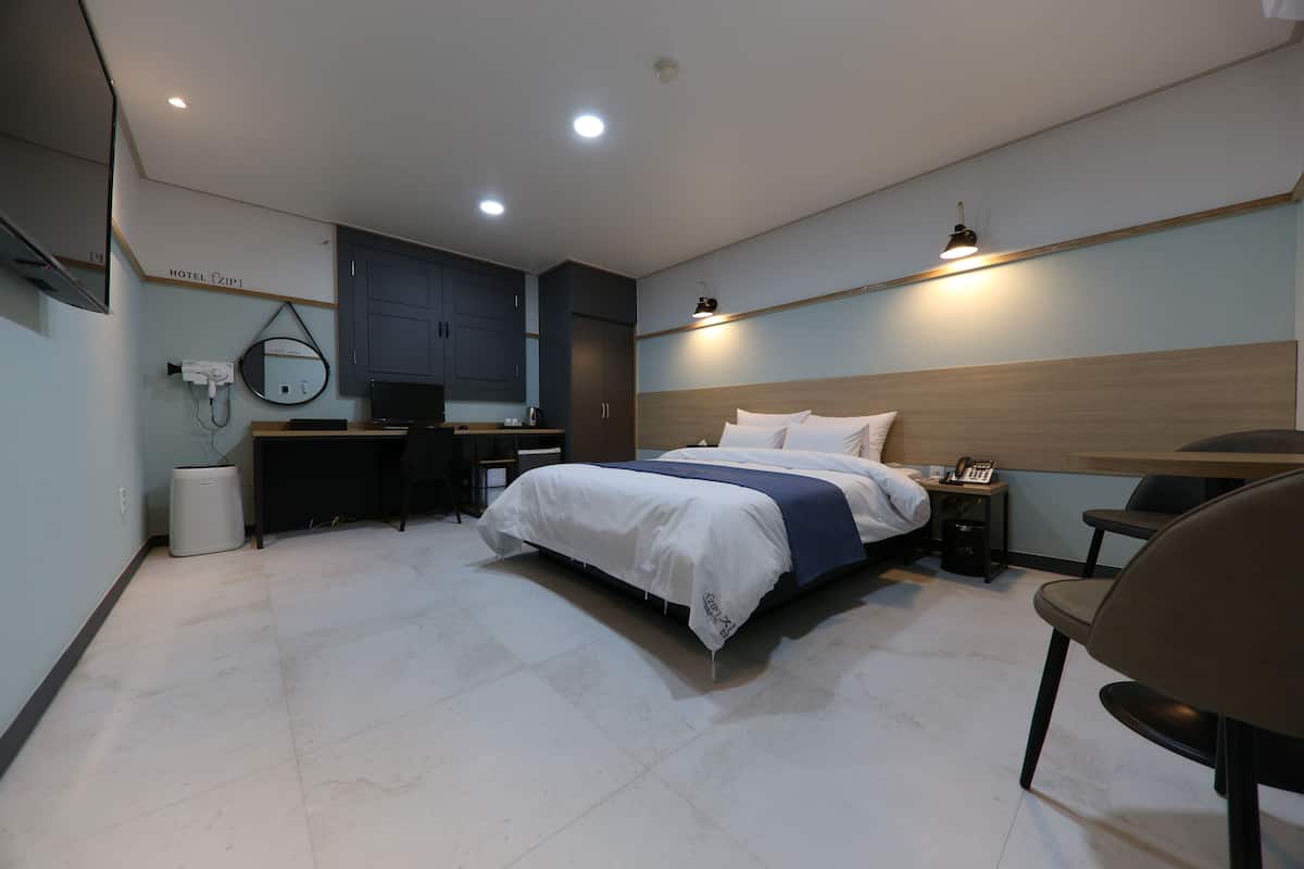 Una habitación de hotel moderna con cama, mesita de noche, silla, escritorio y espejo.