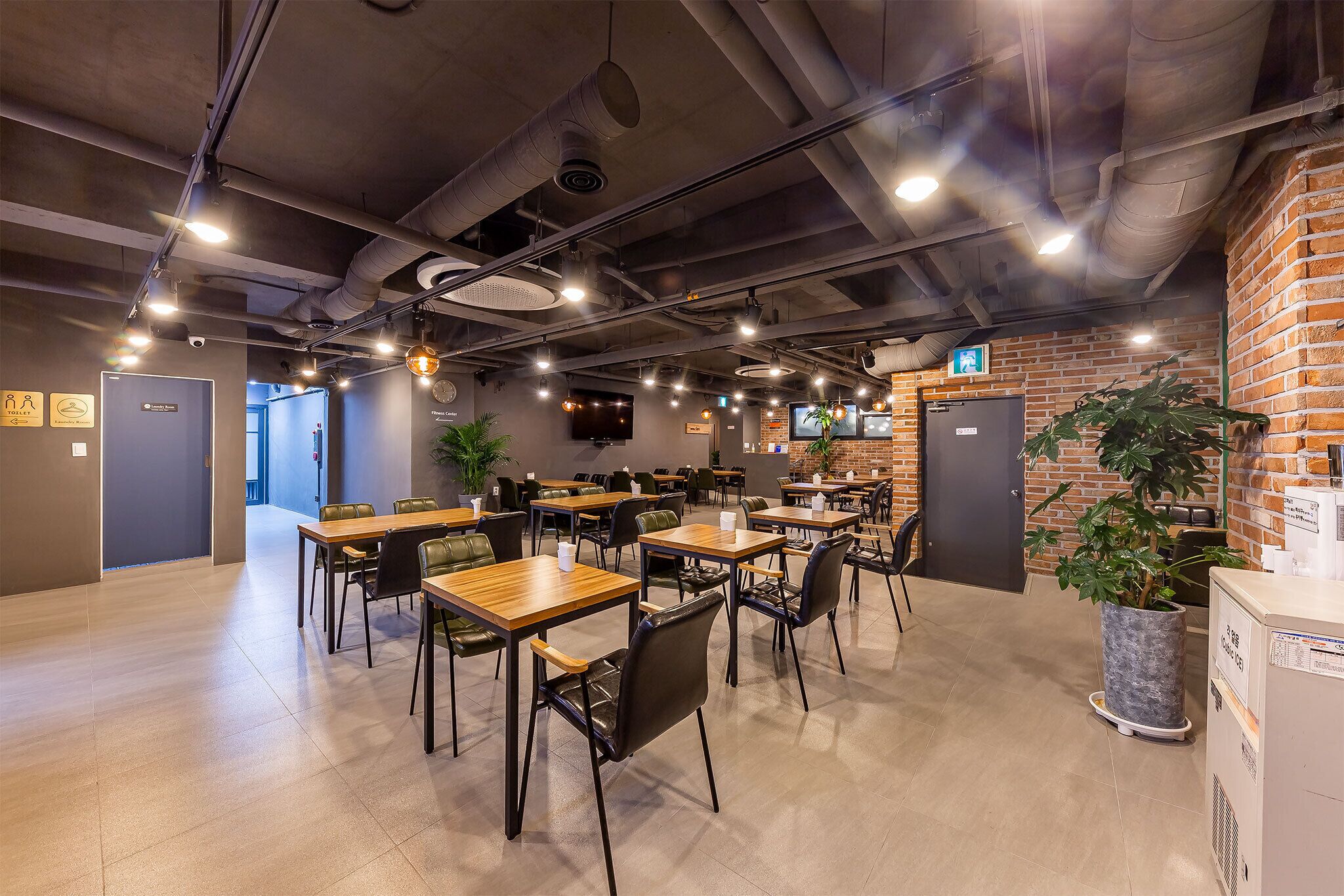 A modern dining area with multiple tables and chairs, a brick wall, and ceiling lights.